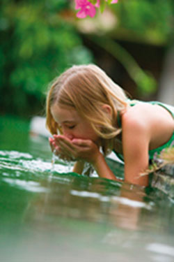 Little girl drinks water from a pond