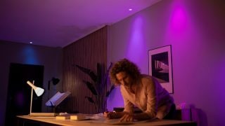 A person is bent over a desk at home, in a room with colourful ambient lighting